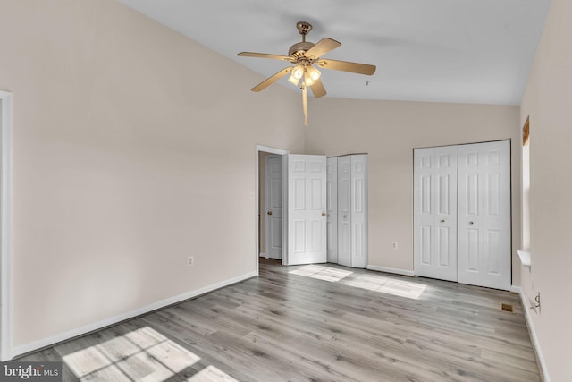 unfurnished bedroom featuring two closets, high vaulted ceiling, light wood-type flooring, and ceiling fan