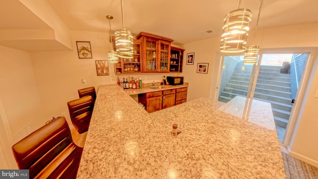 kitchen with kitchen peninsula, light stone countertops, decorative light fixtures, and a kitchen bar