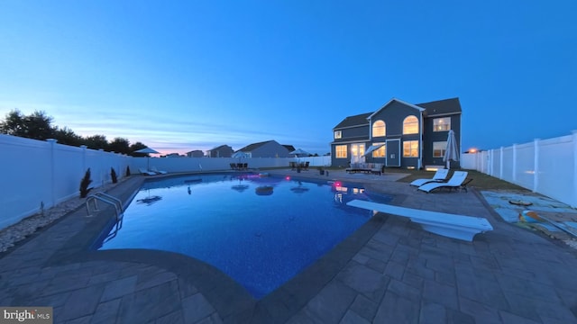 pool at dusk with a diving board and a patio