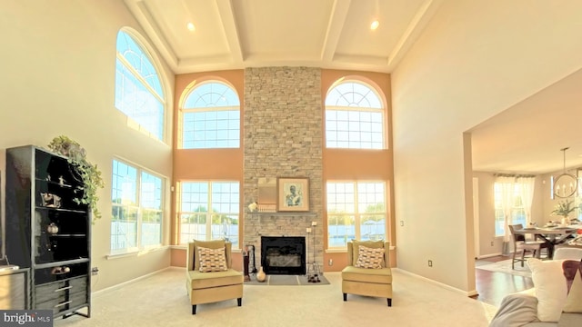 carpeted living room with a wealth of natural light, beamed ceiling, a stone fireplace, and a towering ceiling