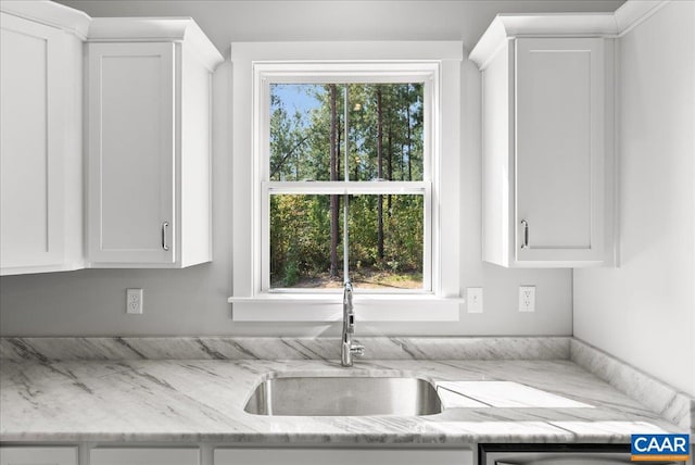 kitchen with white cabinetry, light stone counters, and sink