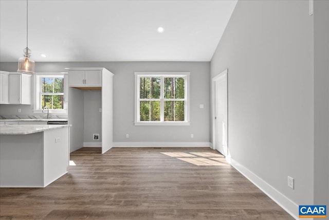 kitchen with hardwood / wood-style floors, white cabinetry, vaulted ceiling, decorative light fixtures, and light stone counters