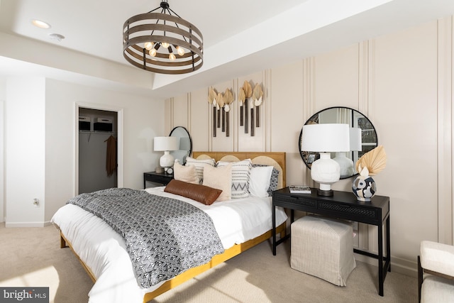 bedroom with a raised ceiling, a walk in closet, an inviting chandelier, carpet flooring, and a closet