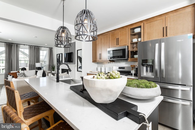 kitchen with stainless steel appliances, a center island with sink, sink, a notable chandelier, and decorative light fixtures