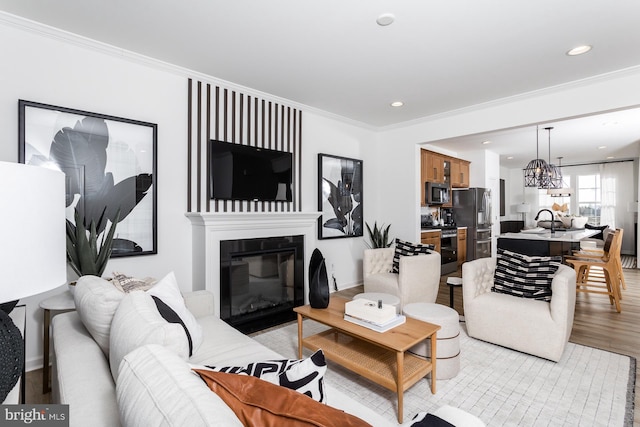 living room with sink, crown molding, a notable chandelier, and light wood-type flooring