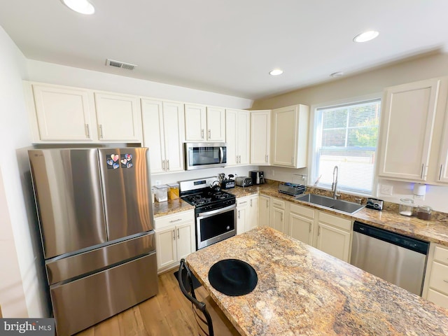 kitchen with light stone countertops, appliances with stainless steel finishes, sink, light wood-type flooring, and white cabinetry