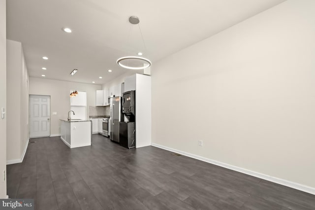 interior space featuring white cabinetry, stainless steel fridge, a kitchen island with sink, and pendant lighting