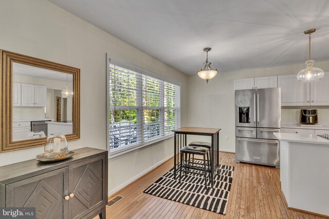 kitchen with white cabinetry, light hardwood / wood-style floors, stainless steel fridge with ice dispenser, and hanging light fixtures