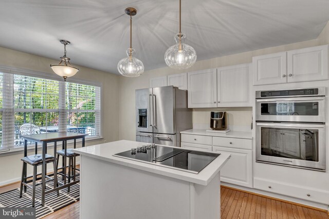 kitchen featuring appliances with stainless steel finishes, a kitchen island, white cabinetry, light hardwood / wood-style floors, and decorative light fixtures