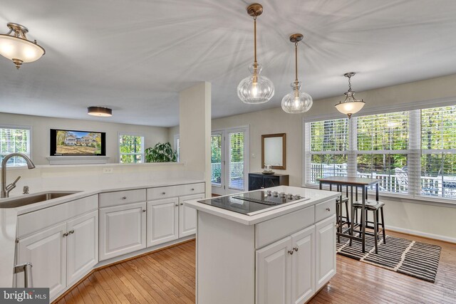 kitchen featuring black electric stovetop, sink, light wood-type flooring, a center island, and white cabinets