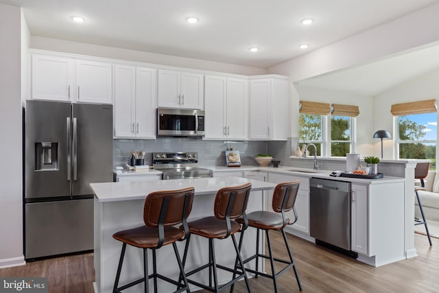 kitchen featuring hardwood / wood-style floors, sink, a center island, white cabinetry, and appliances with stainless steel finishes