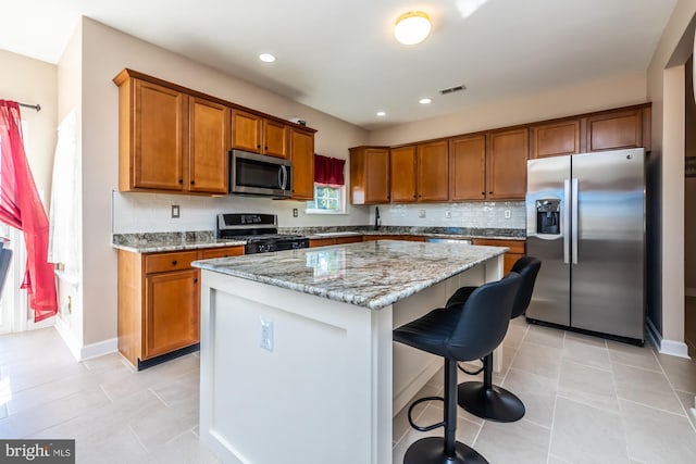 kitchen with appliances with stainless steel finishes, a center island, a kitchen breakfast bar, light stone counters, and decorative backsplash