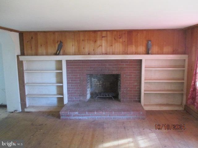 interior details with wood-type flooring, wooden walls, and a brick fireplace