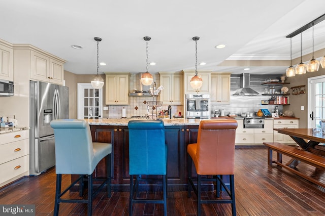 kitchen featuring cream cabinets, stainless steel appliances, dark wood-type flooring, and wall chimney range hood