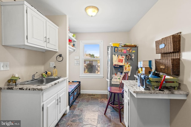 kitchen with white cabinets, stainless steel fridge, light stone countertops, and sink