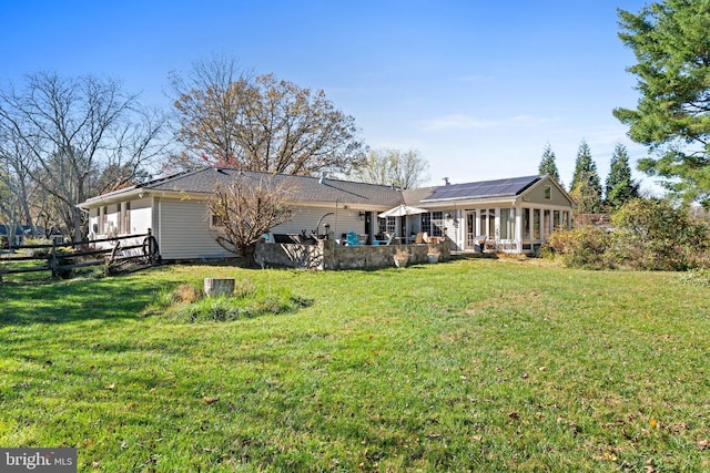 back of property with a sunroom, solar panels, and a lawn