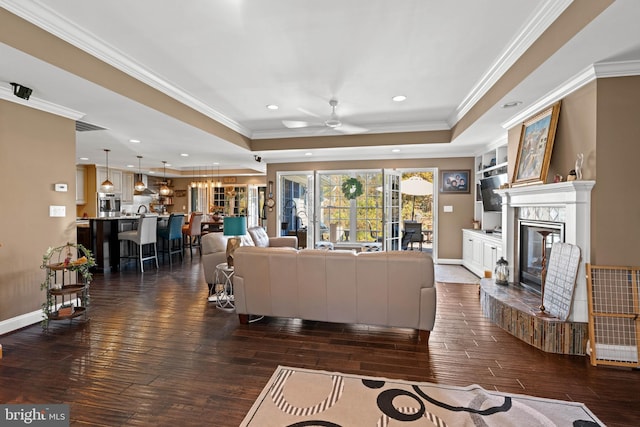 living room with a tray ceiling, ceiling fan, dark hardwood / wood-style floors, and ornamental molding