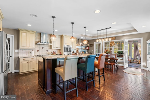 kitchen featuring dark wood-type flooring, pendant lighting, stainless steel appliances, and wall chimney exhaust hood