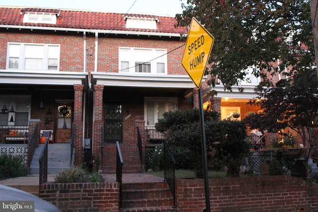 multi unit property with brick siding, a porch, and mansard roof