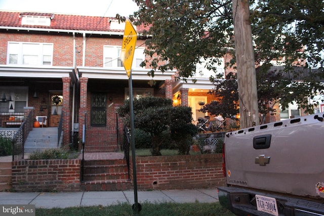 multi unit property featuring brick siding, a porch, a tiled roof, and mansard roof