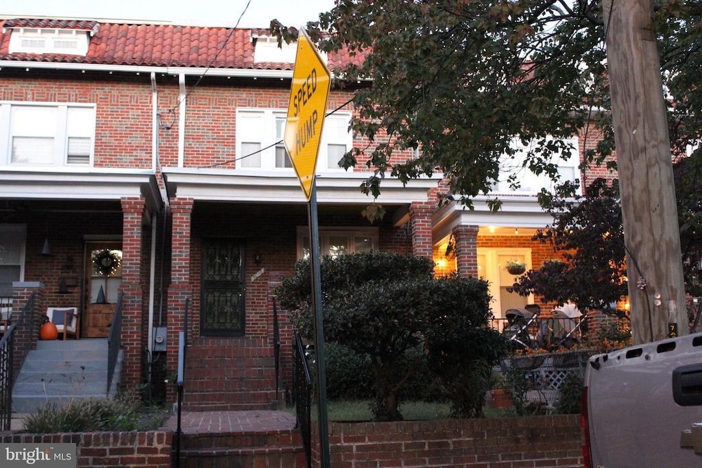 view of property with brick siding, covered porch, a tile roof, and mansard roof