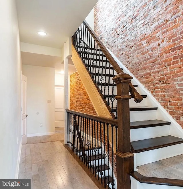 stairs featuring hardwood / wood-style flooring and brick wall