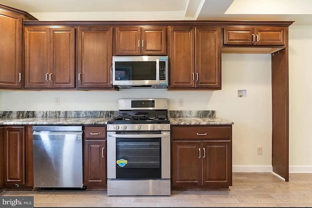 kitchen with appliances with stainless steel finishes, light hardwood / wood-style flooring, and dark stone counters