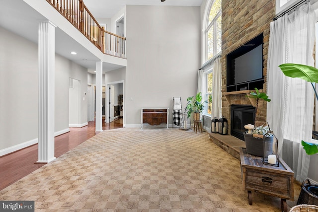 living room featuring ornate columns, a stone fireplace, a towering ceiling, and hardwood / wood-style floors