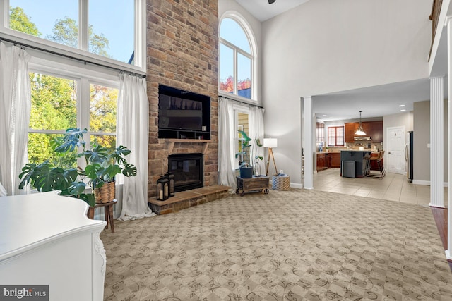 tiled living room featuring a towering ceiling, a healthy amount of sunlight, and a stone fireplace