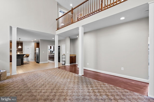 unfurnished living room with light hardwood / wood-style flooring, a high ceiling, and decorative columns