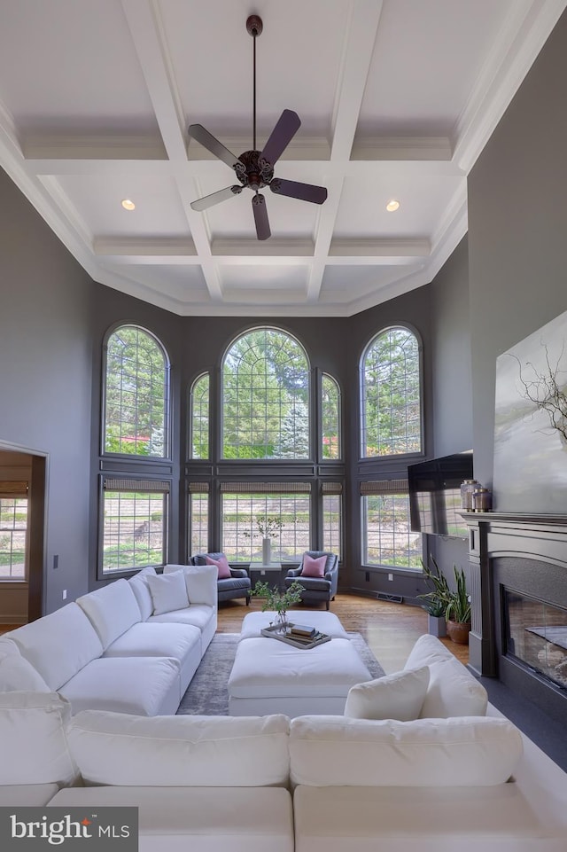 living room with coffered ceiling, hardwood / wood-style flooring, a high ceiling, beamed ceiling, and ceiling fan