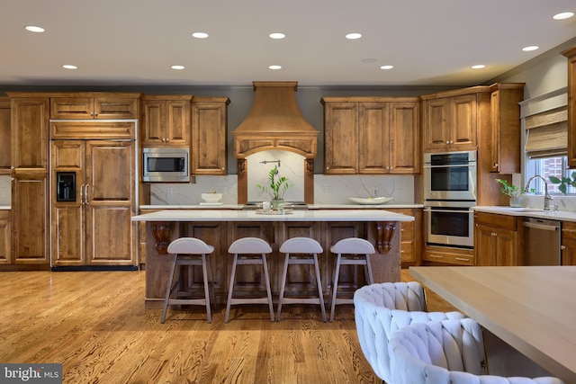 kitchen with built in appliances, sink, light wood-type flooring, and a kitchen island