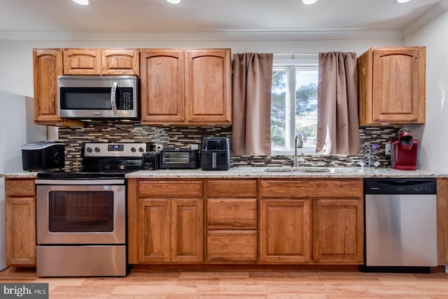 kitchen featuring tasteful backsplash, sink, light hardwood / wood-style floors, stainless steel appliances, and crown molding