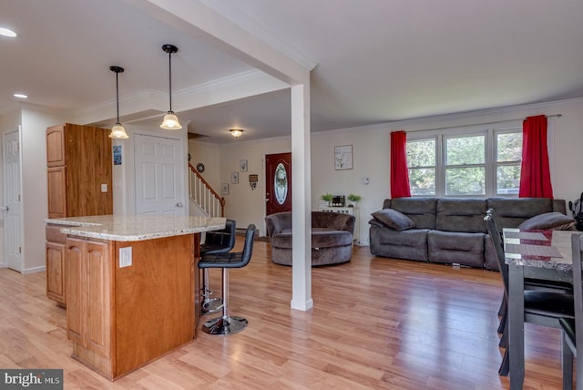 kitchen with light wood-type flooring, a kitchen island, decorative light fixtures, light stone counters, and ornamental molding