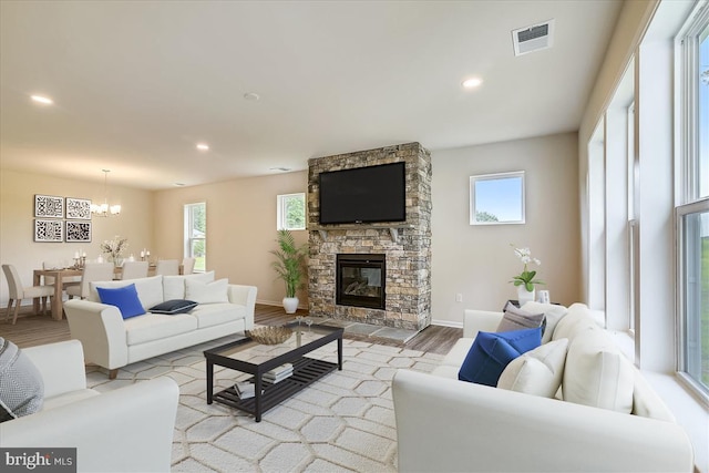 living room featuring a stone fireplace, an inviting chandelier, and light wood-type flooring