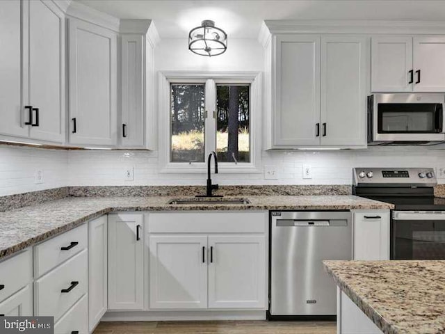 kitchen featuring sink, light stone countertops, white cabinetry, appliances with stainless steel finishes, and tasteful backsplash