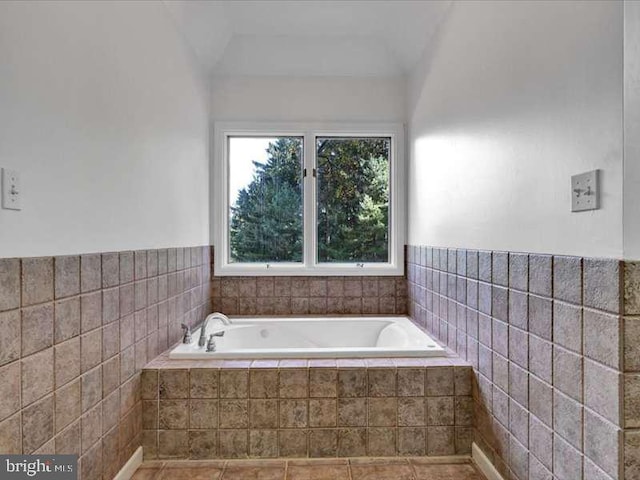 bathroom featuring tile patterned flooring, tiled tub, tile walls, and vaulted ceiling