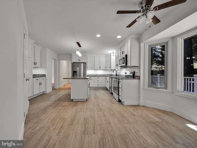 kitchen with a kitchen island, hanging light fixtures, stainless steel appliances, light wood-type flooring, and white cabinets