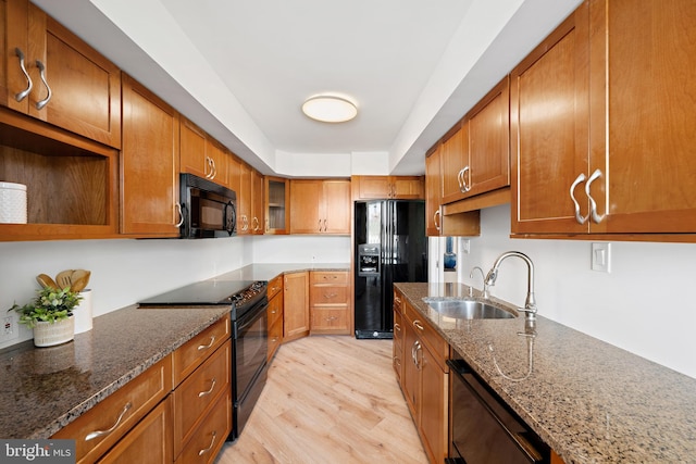 kitchen featuring dark stone countertops, sink, black appliances, and light hardwood / wood-style floors