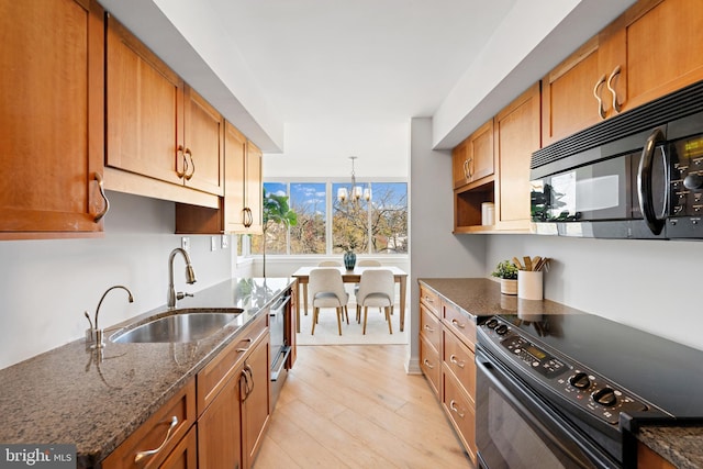 kitchen featuring sink, a notable chandelier, dark stone countertops, appliances with stainless steel finishes, and light wood-type flooring