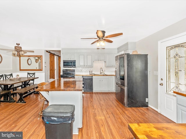 kitchen with black appliances, light wood-type flooring, a barn door, wood counters, and sink