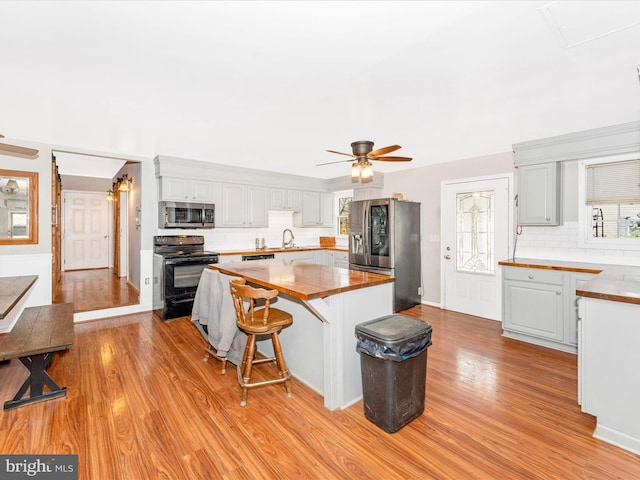 kitchen with wooden counters, stainless steel appliances, decorative backsplash, ceiling fan, and light hardwood / wood-style flooring