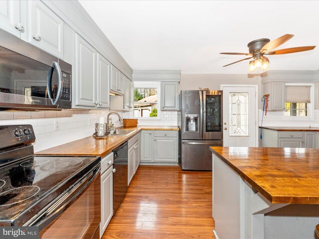 kitchen with butcher block counters, sink, black appliances, light wood-type flooring, and decorative backsplash