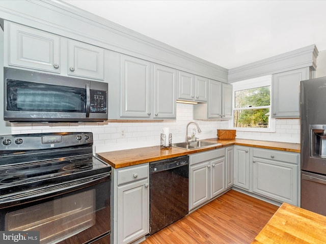 kitchen with light wood-type flooring, butcher block countertops, black appliances, and sink