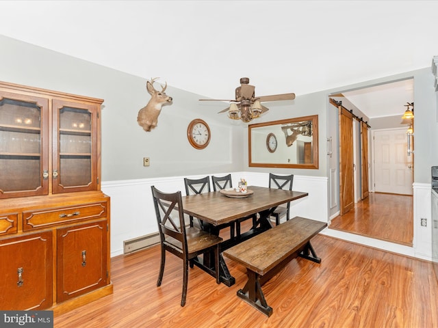 dining room featuring a baseboard radiator, light hardwood / wood-style floors, a barn door, and ceiling fan