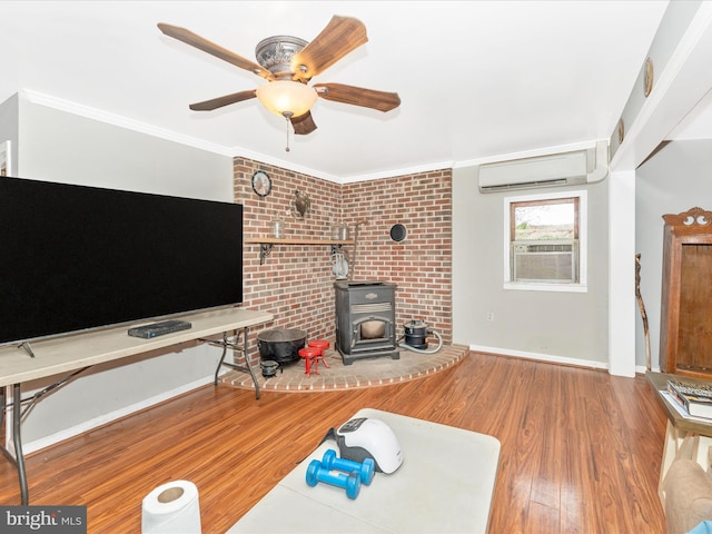 living room featuring crown molding, a wood stove, hardwood / wood-style flooring, a wall mounted air conditioner, and ceiling fan