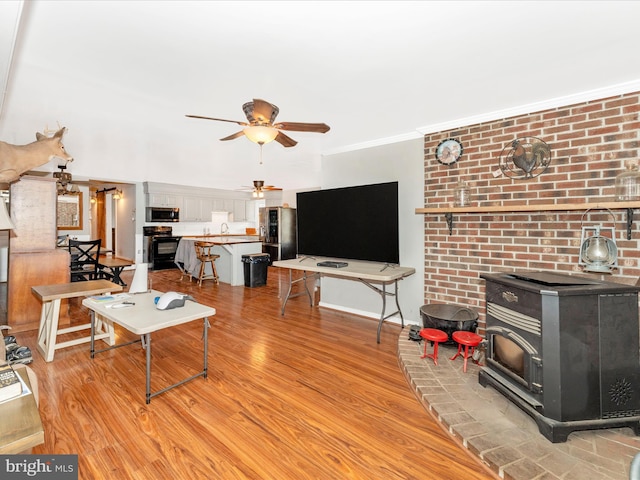 living room featuring ornamental molding, light hardwood / wood-style flooring, a wood stove, and ceiling fan