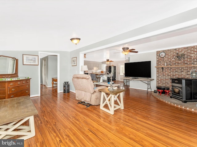 living room with a wood stove, light wood-type flooring, and ceiling fan