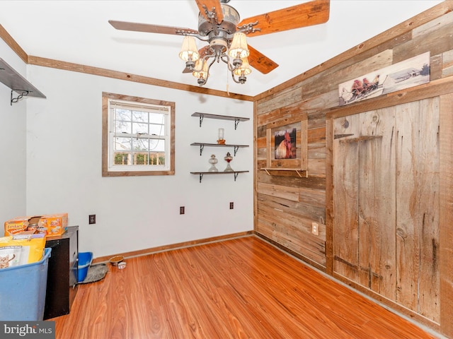 spare room with ornamental molding, light hardwood / wood-style flooring, wood walls, and ceiling fan