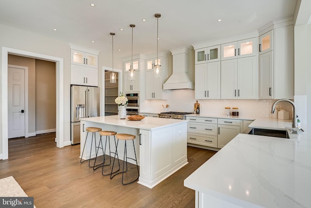 kitchen featuring white cabinetry, custom range hood, stainless steel appliances, sink, and a center island